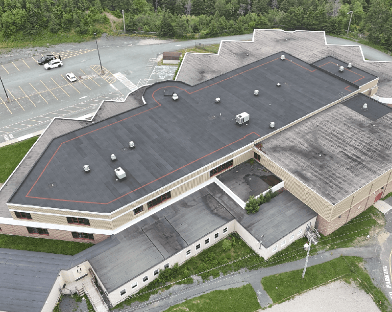 Aerial view of a large single-story building with a dark roof and surrounding parking lot Aerial view of a large single-story building with a dark roof and surrounding parking lot